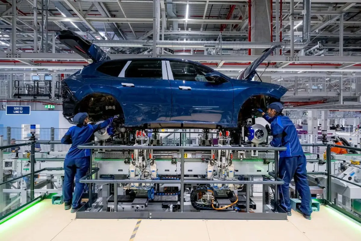 Blue sedan on a factory assembly line with technicians working nearby Blue sedan on a factory assembly line with technicians working nearby